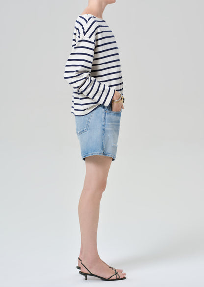 Person wearing a striped shirt and denim shorts on a grey background