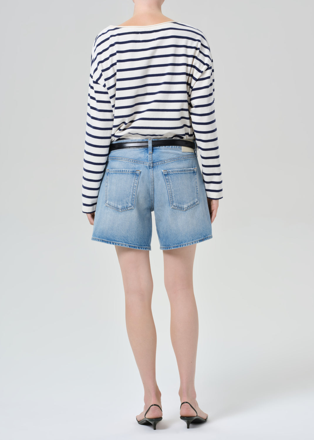 Person wearing a striped shirt and denim shorts on a grey background