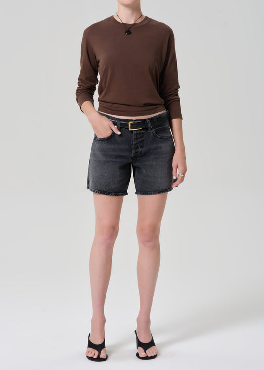 Person wearing a brown long-sleeve top and black denim shorts on a grey background