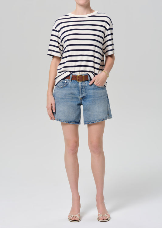 Person wearing a striped shirt and denim shorts on a grey background