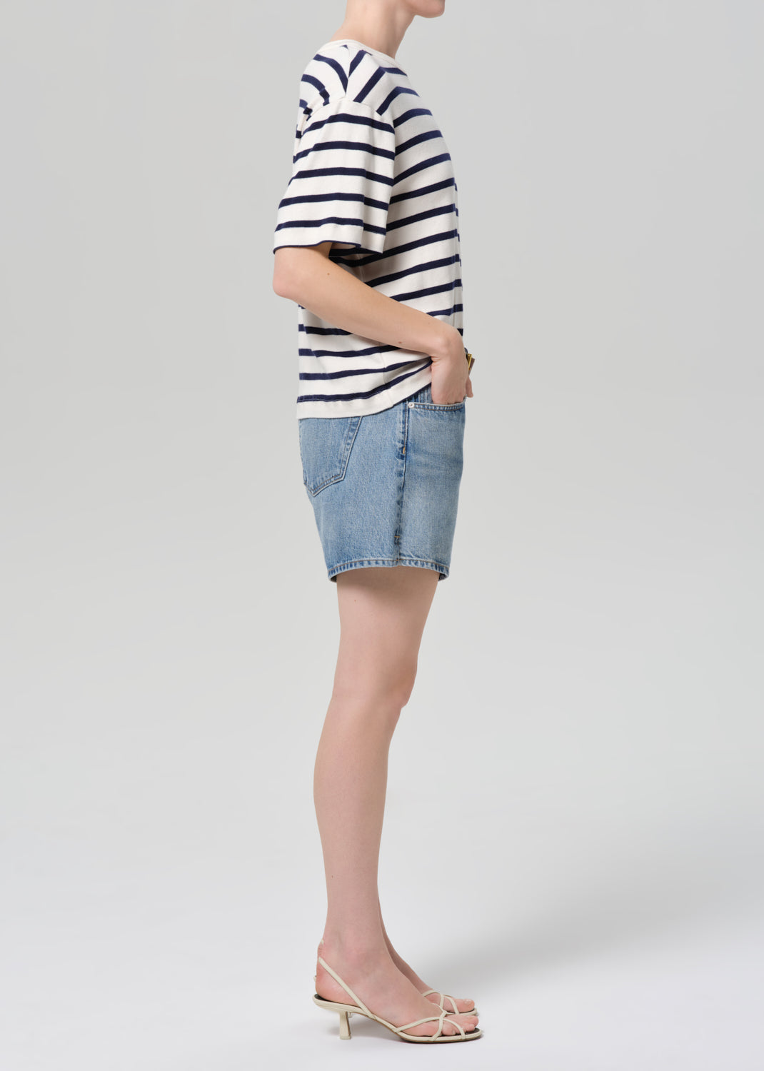 Person wearing a striped shirt and denim short on a plain background