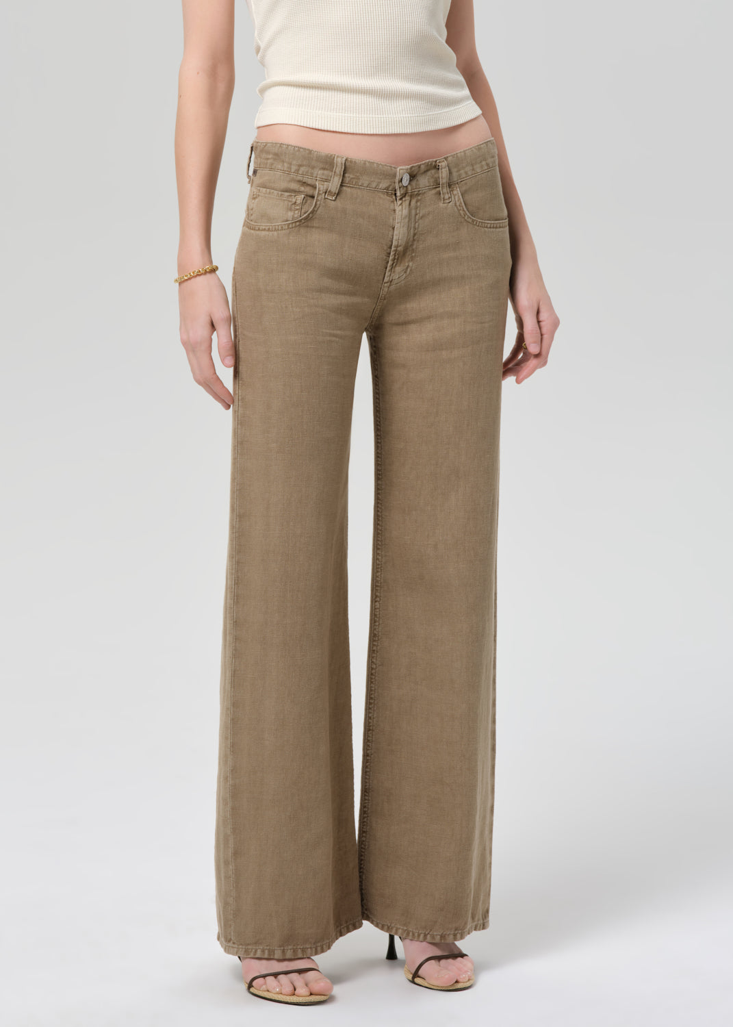 Person wearing a off-white sleeveless top and wide-leg brown linen pants on a plain background