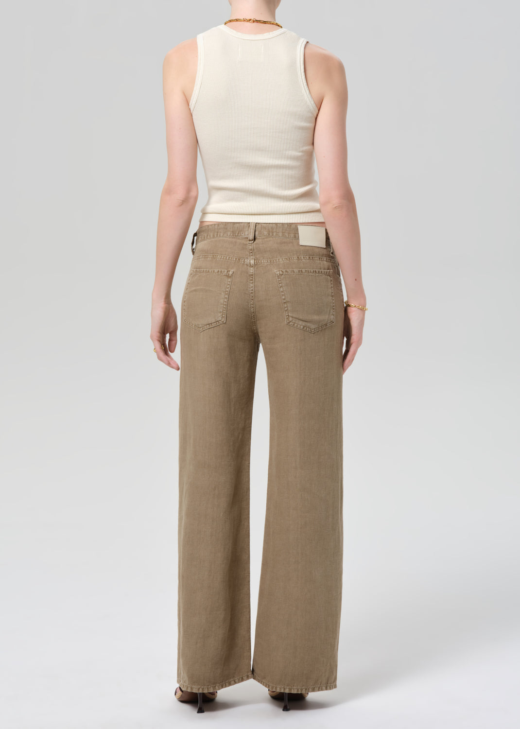 Person wearing a off-white sleeveless top and wide-leg brown linen pants on a plain background