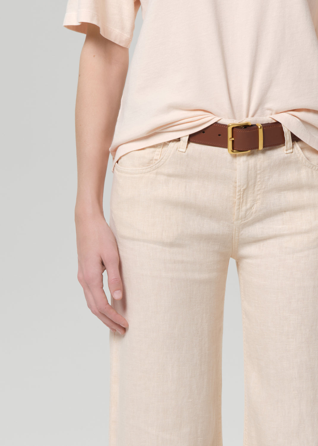 Person wearing a light peach top and off-white linen wide-leg pants on a plain background