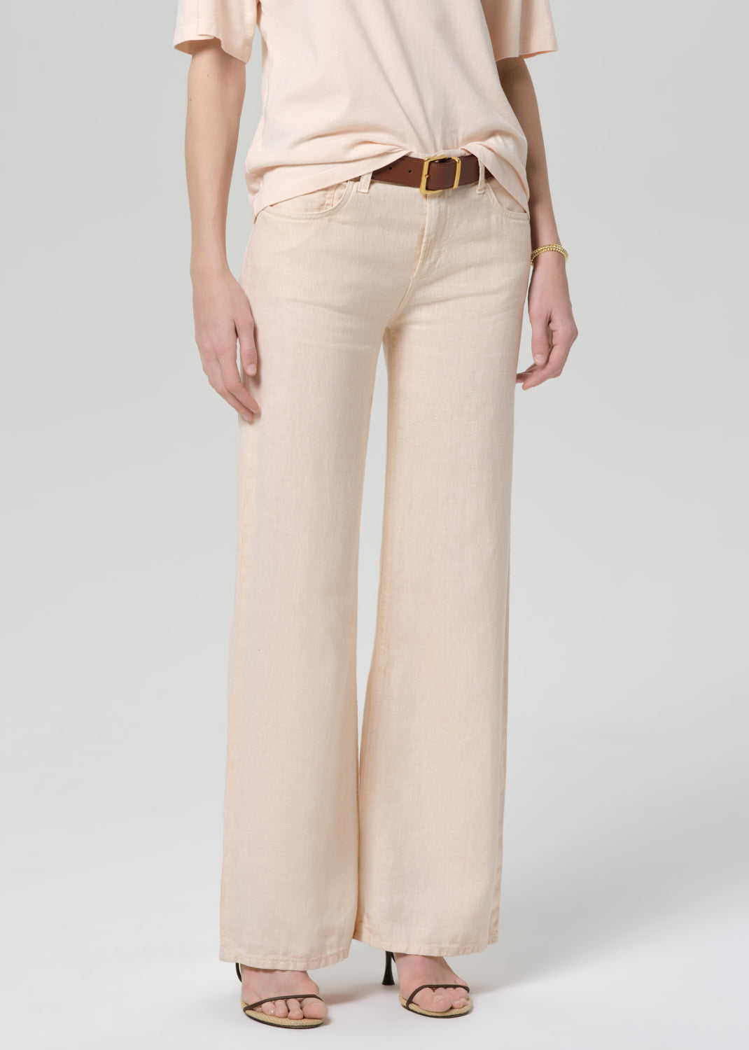 Person wearing a light peach top and off-white linen wide-leg pants on a plain background