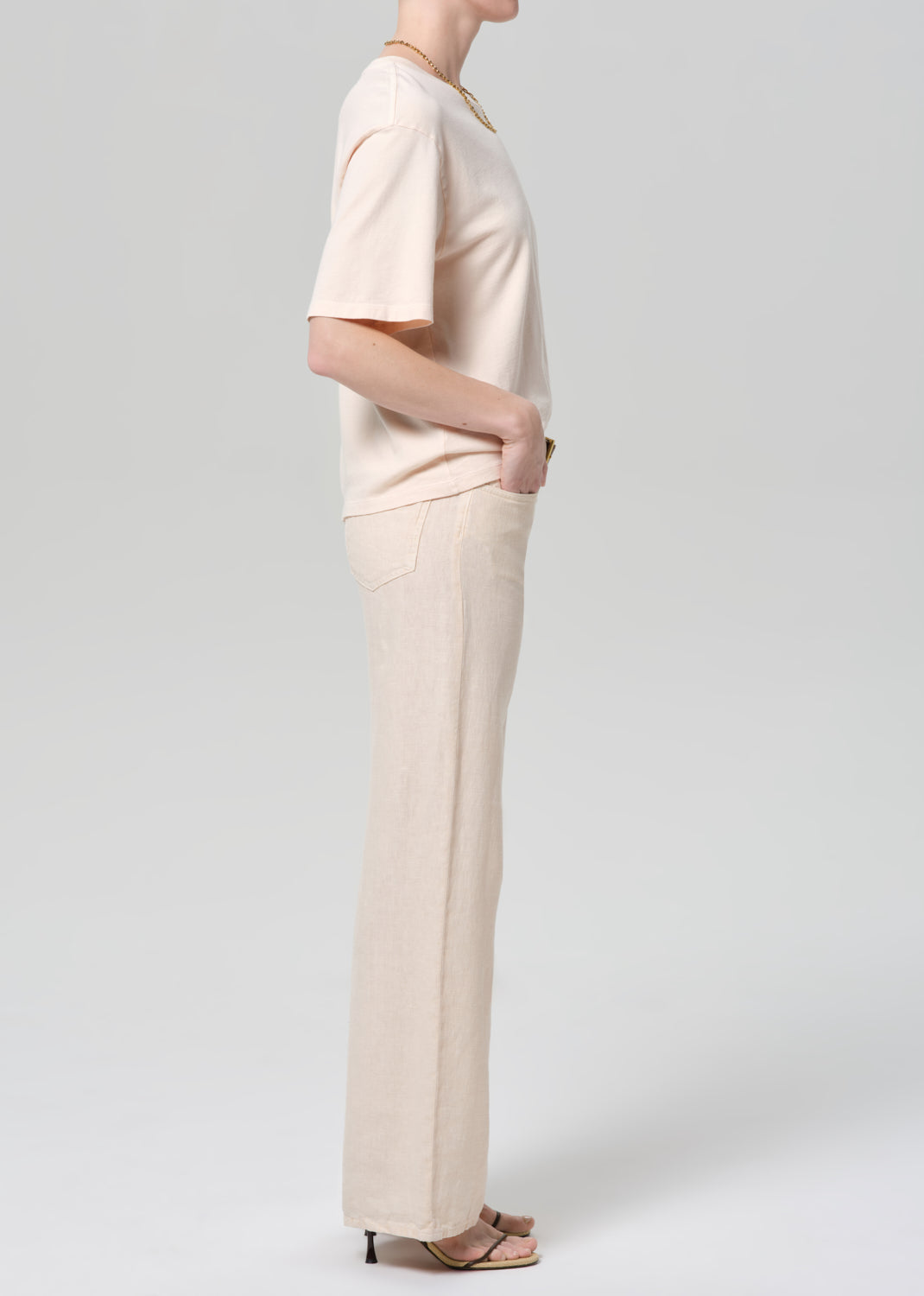 Person wearing a light peach top and off-white linen wide-leg pants on a plain background