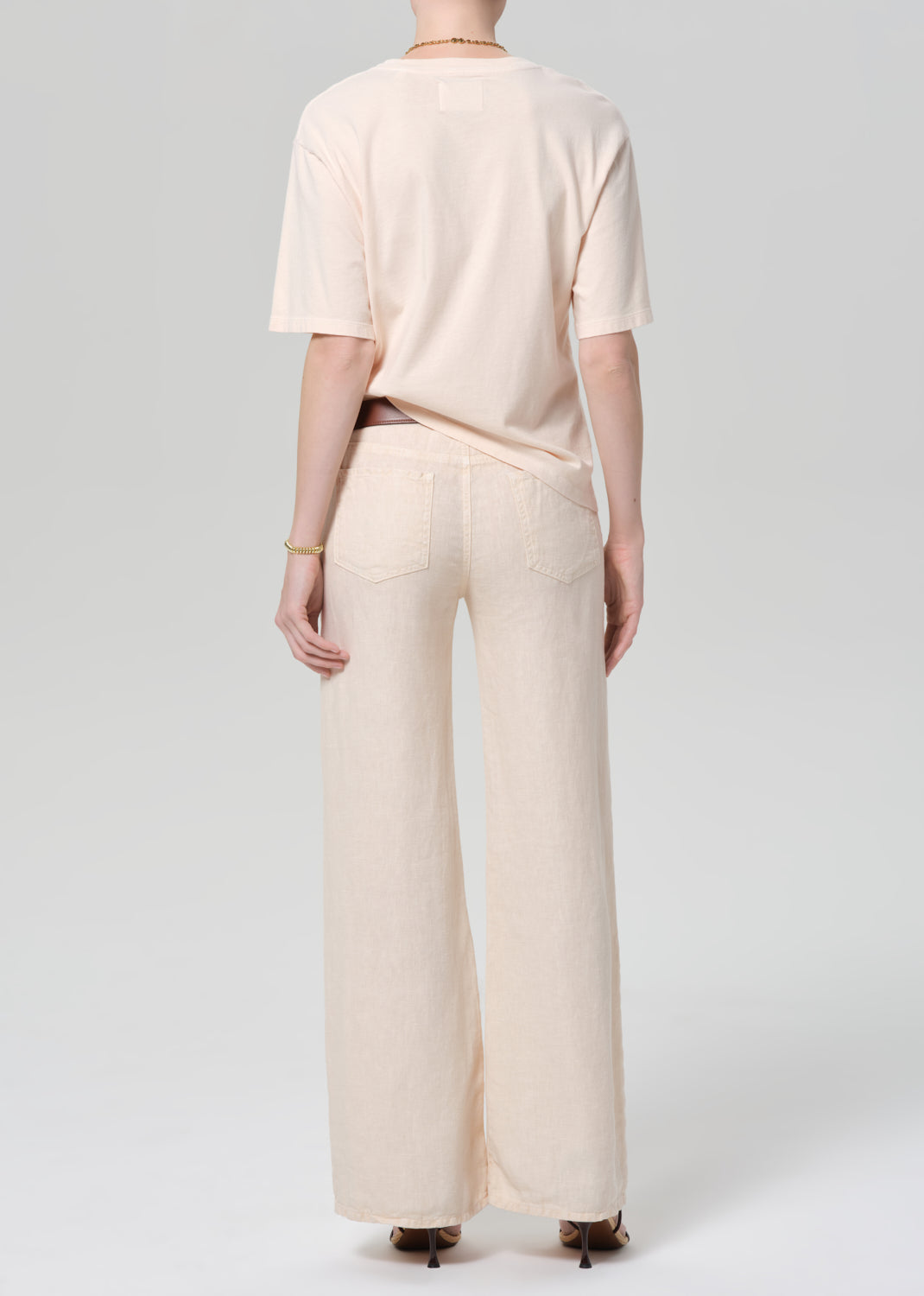 Person wearing a light peach top and off-white linen wide-leg pants on a plain background