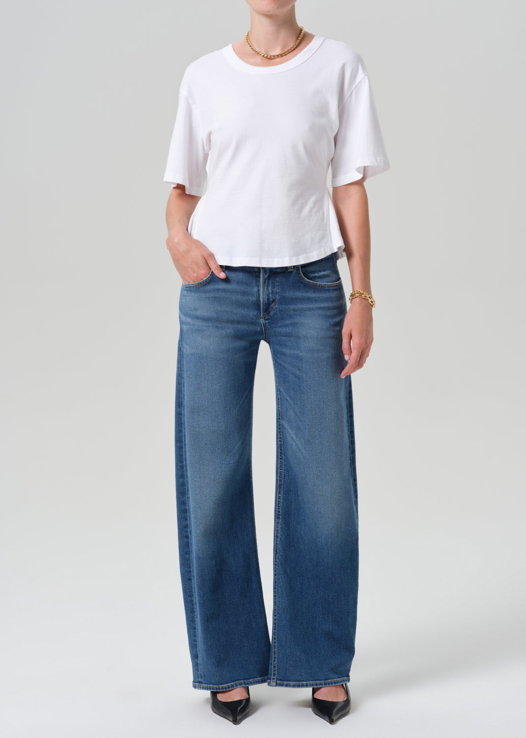 A model wearing a white short-sleeve t-shirt and blue wide-leg jeans, standing against a grey studio background.