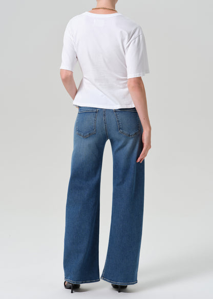 A model shown from the back wearing a white short-sleeve t-shirt and wide-leg blue denim jeans, photographed against a grey background.