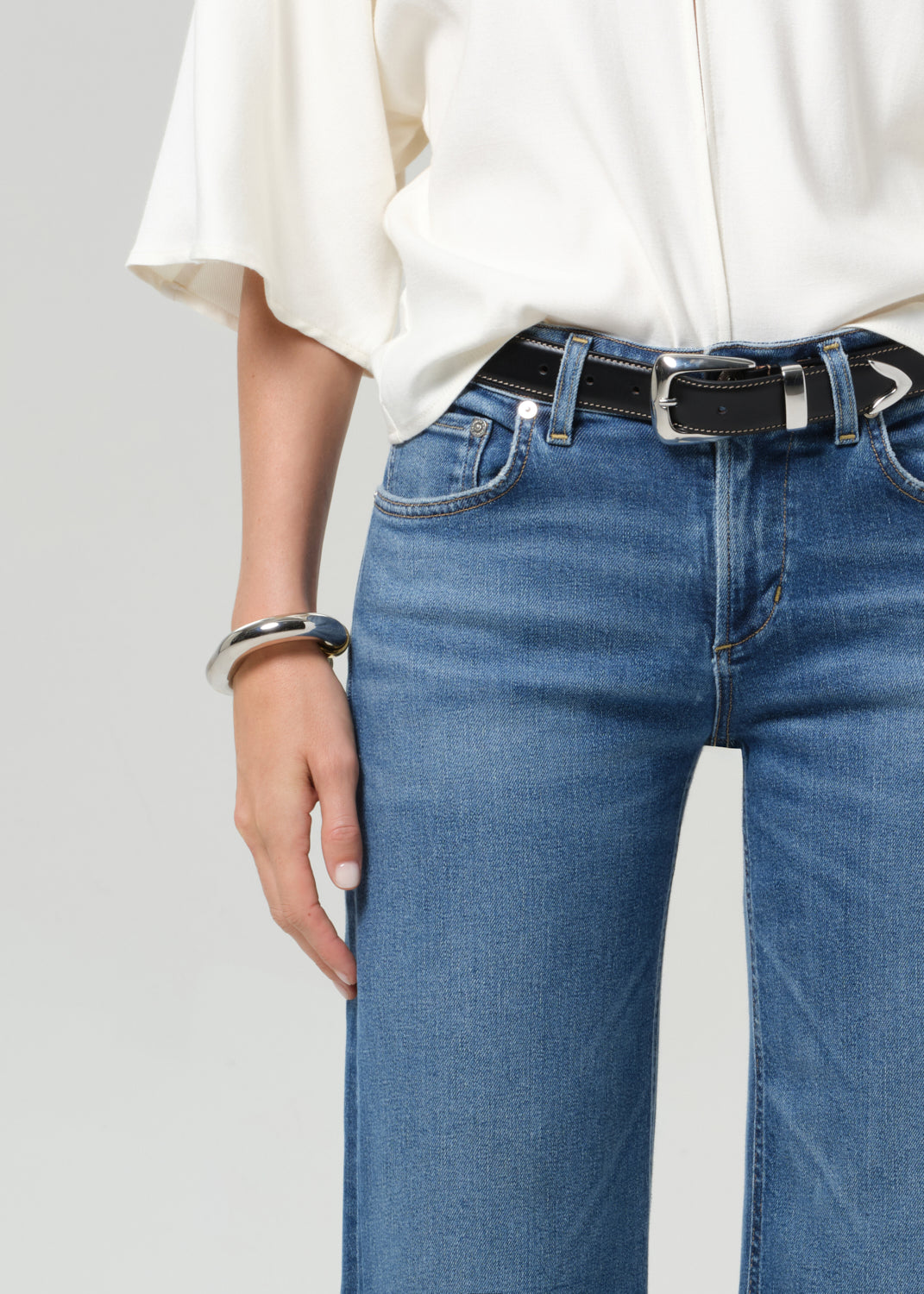 Person wearing a white shirt and blue jeans with a black belt on a gray background