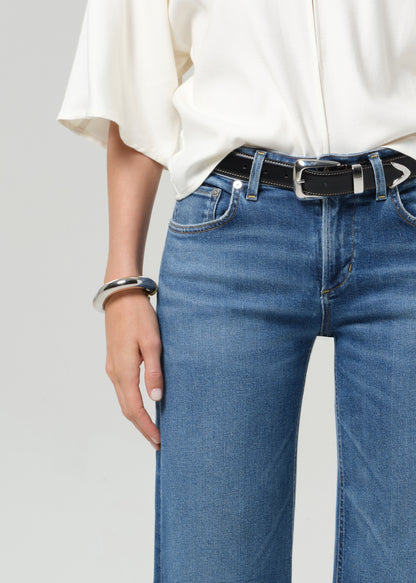 Person wearing a white shirt and blue jeans with a black belt on a gray background