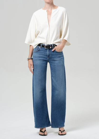 Person wearing a white blouse and blue jeans on a plain background
