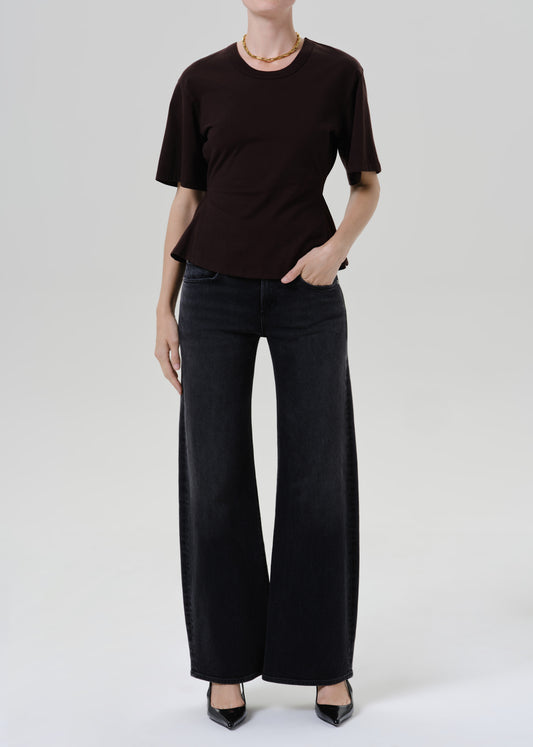 A model wearing a dark brown short-sleeve crewneck top and black wide-leg pants, standing against a grey background.