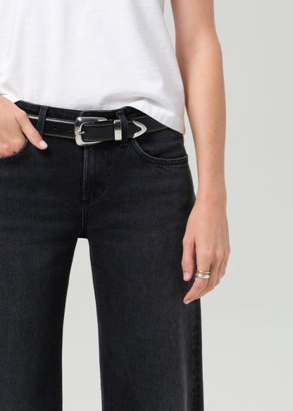 Person wearing black jeans with a belt on a plain background