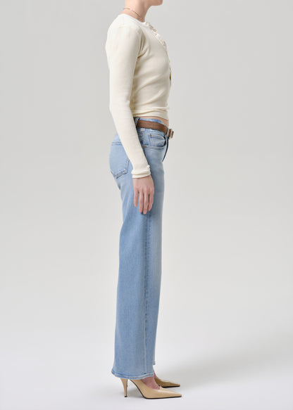 A model shown in profile wearing a cream ribbed long-sleeve top, light-wash wide-leg jeans, and beige pointed-toe heels against a grey background.