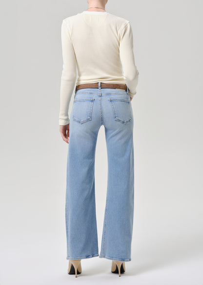 A model shown from the back wearing light-wash wide-leg jeans, a cream long-sleeve top, and black high heels against a grey background.
