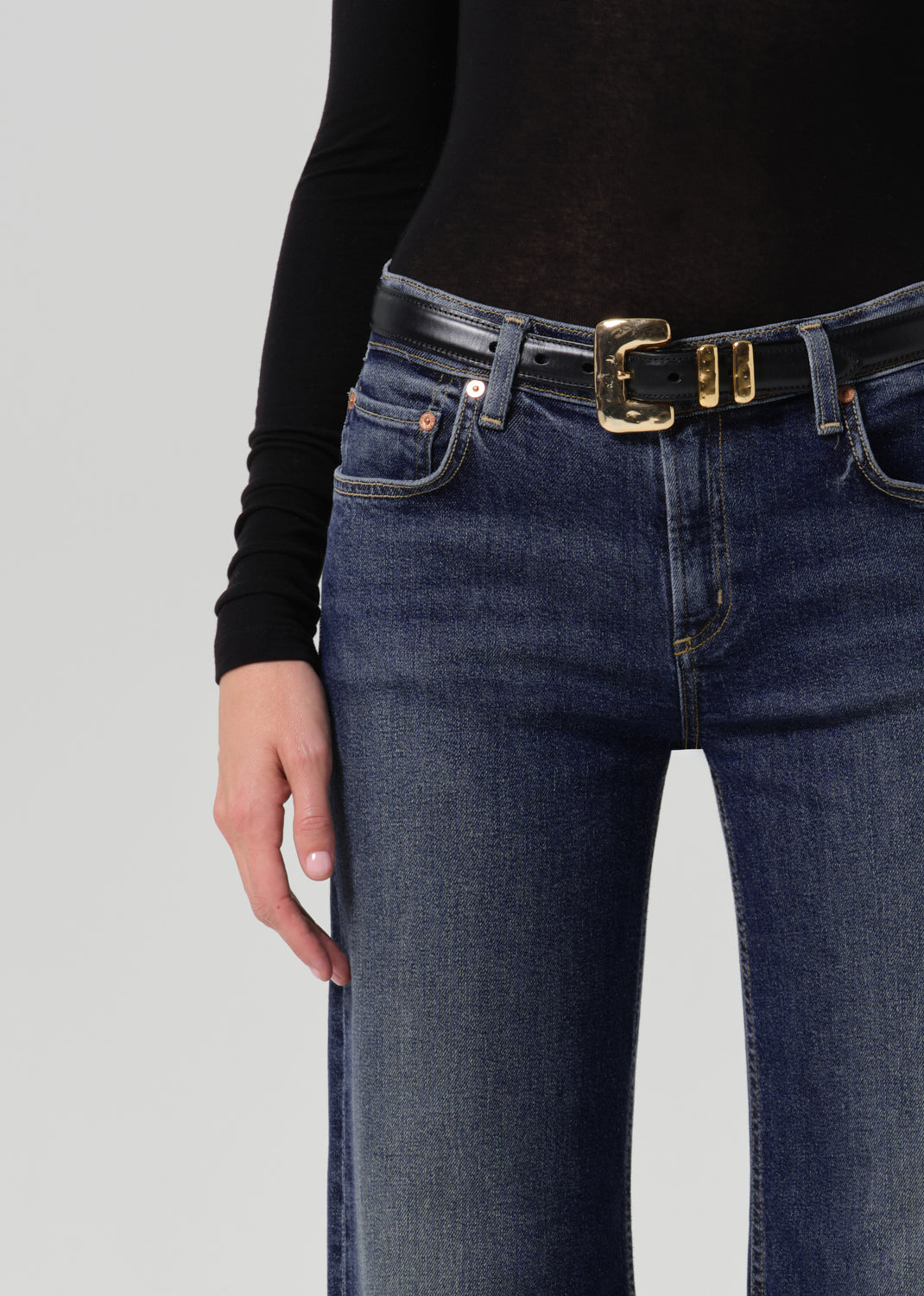 Close-up of dark blue wide leg jeans showing the waistband, front pockets, belt, and subtle fading.