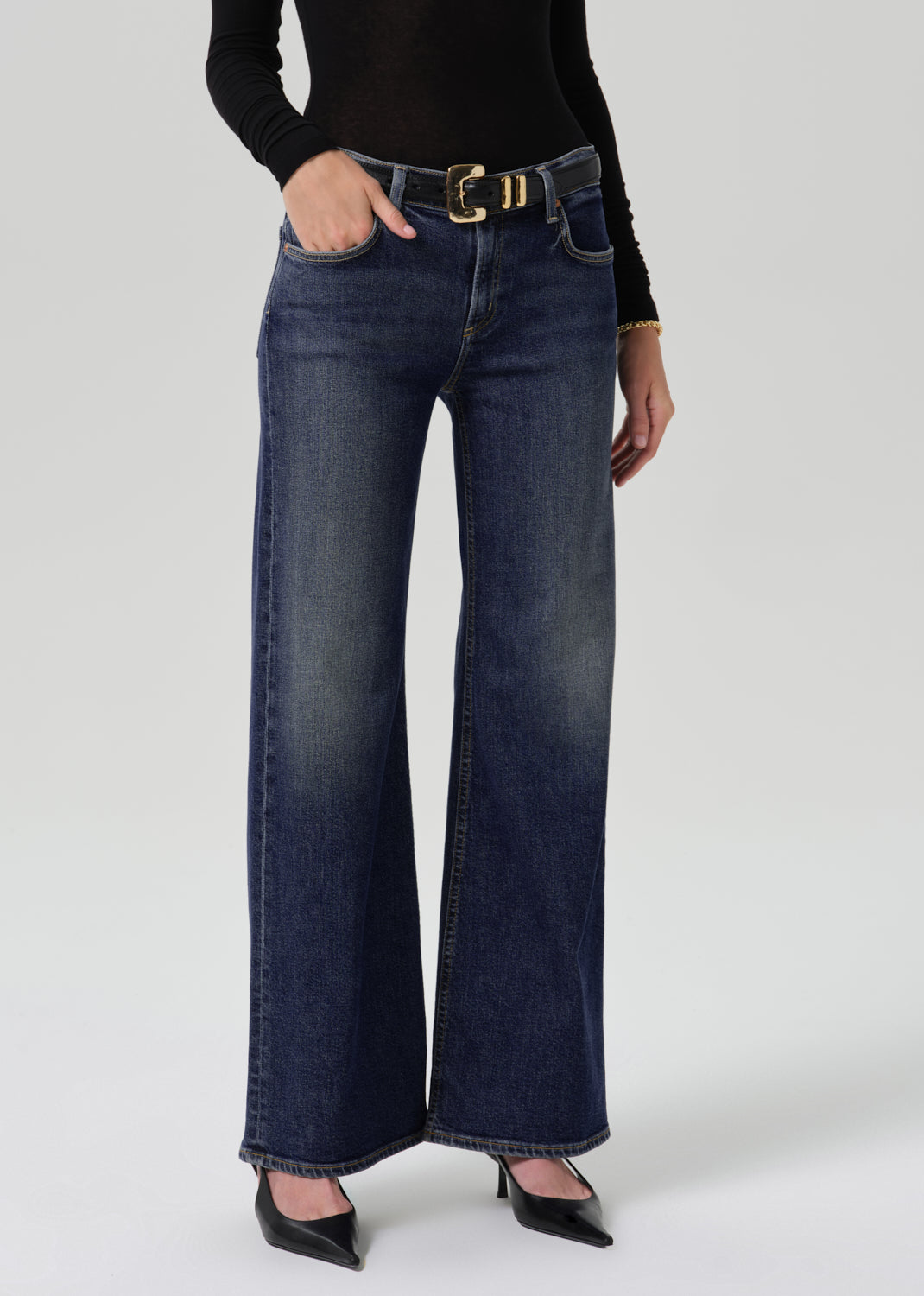 Person wearing dark blue wide leg jeans with a black long sleeve turtleneck top and black heels, front cropped view on a grey background.