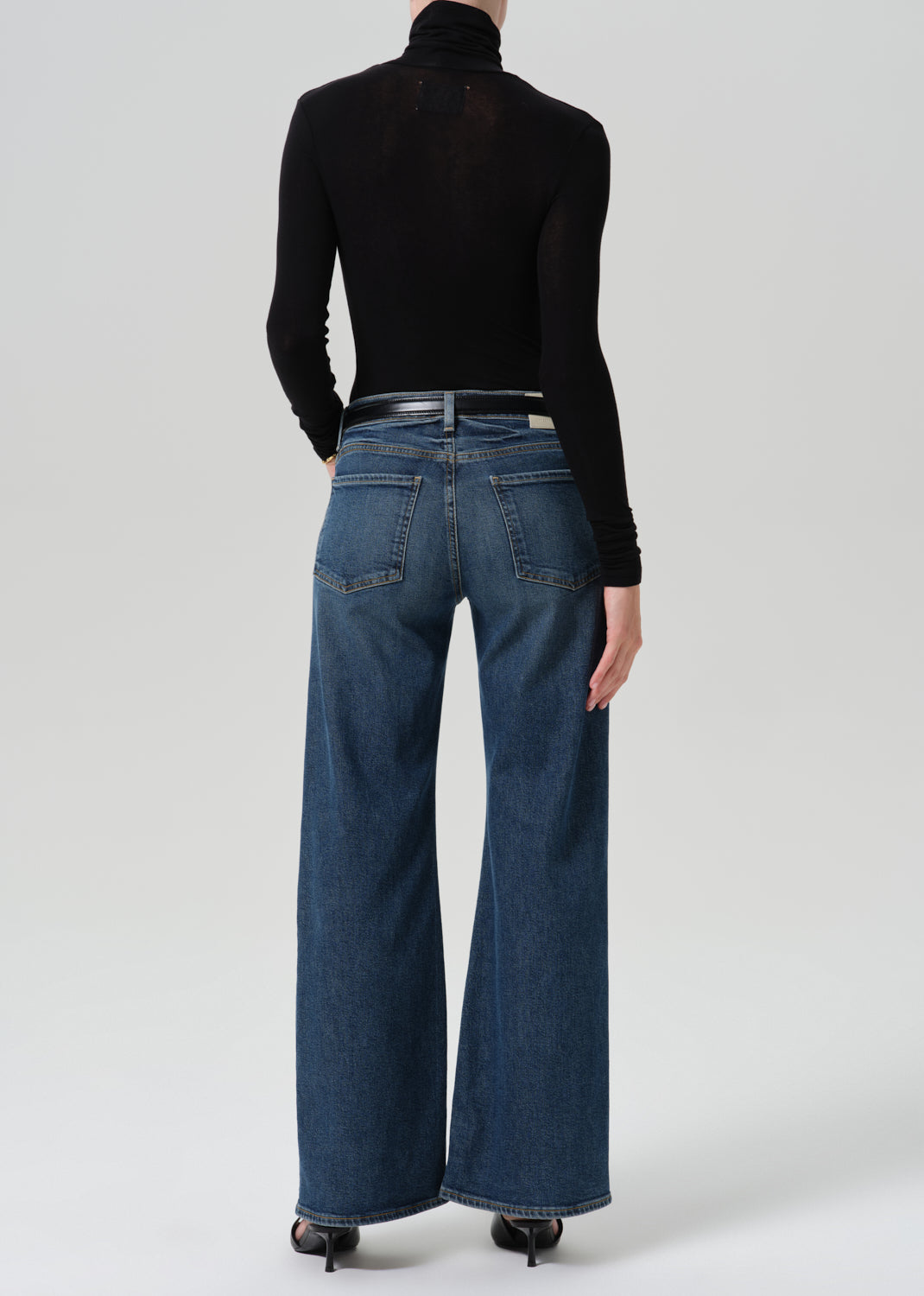 Person wearing black turtleneck with a blue pant on a grey background