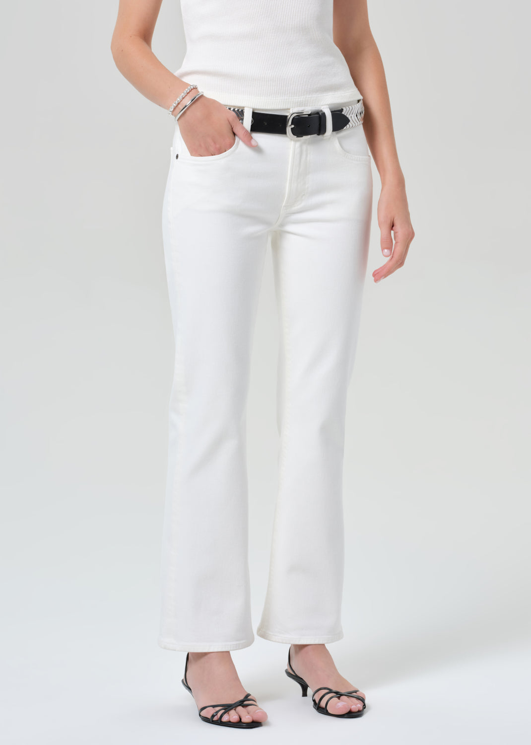 Person wearing white pants with a black belt on a grey background