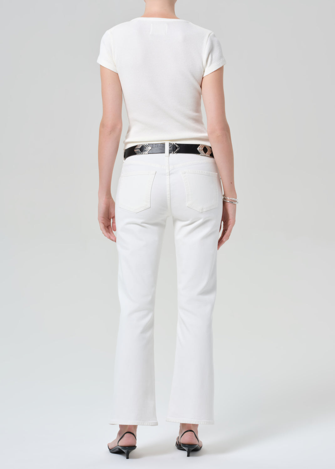 Person wearing a white top and white pants with a black belt on a plain background