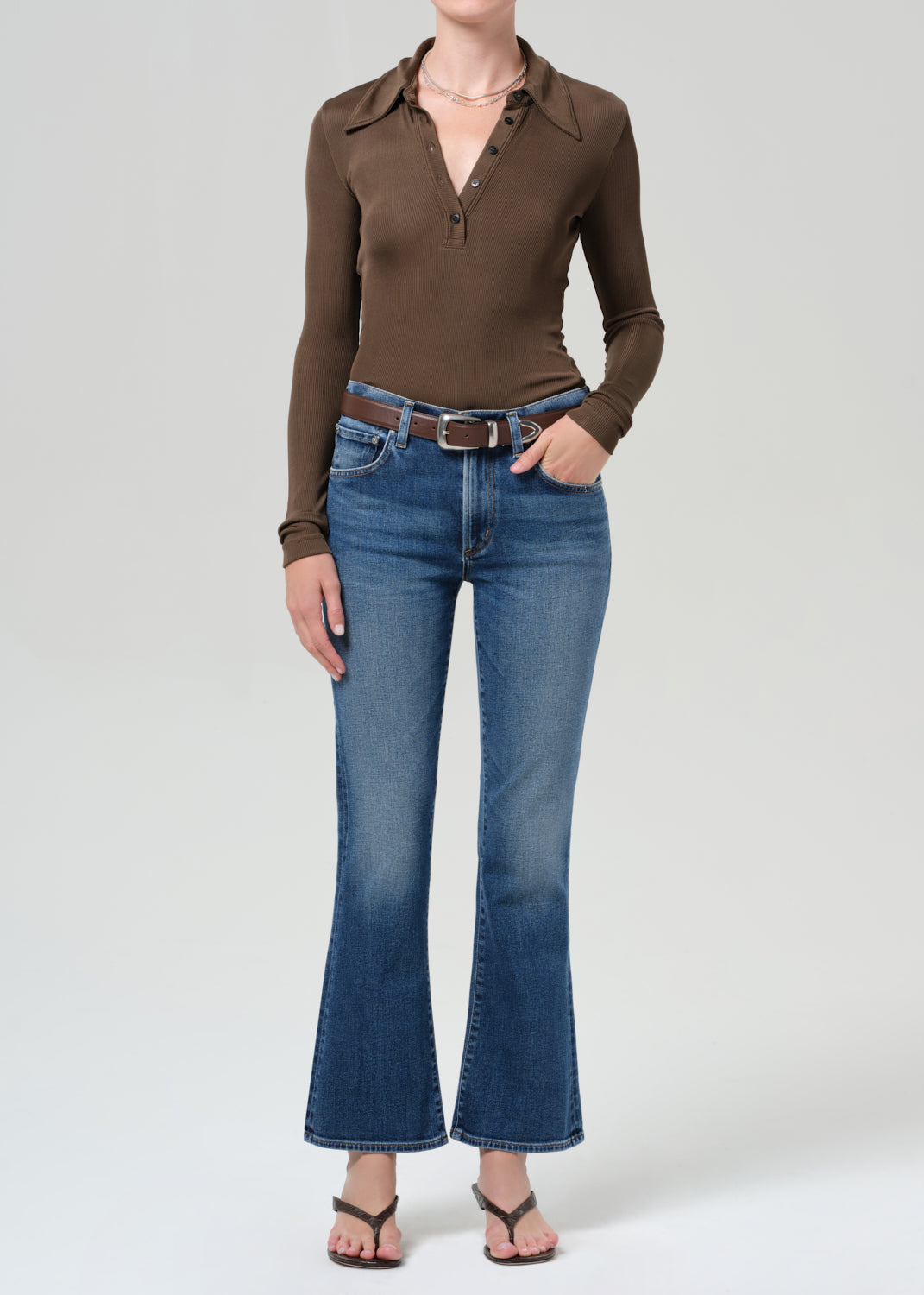 Person wearing a brown long-sleeve shirt and blue jeans on a grey background