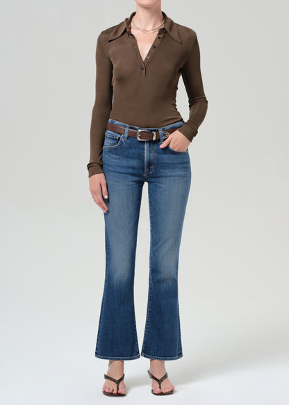 Person wearing a brown long-sleeve shirt and blue jeans on a grey background