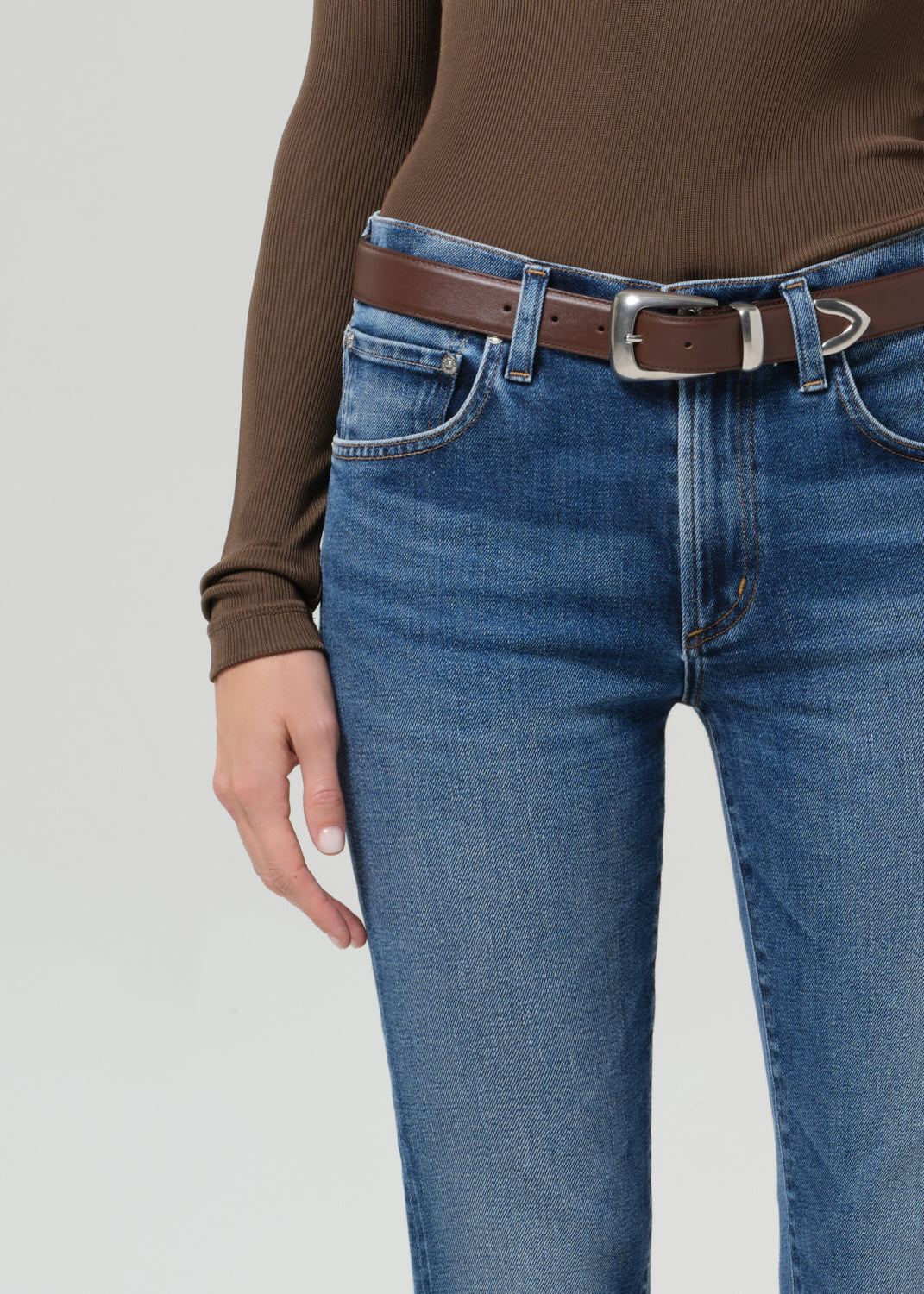 Person wearing a brown long-sleeve shirt and blue jeans on a grey background