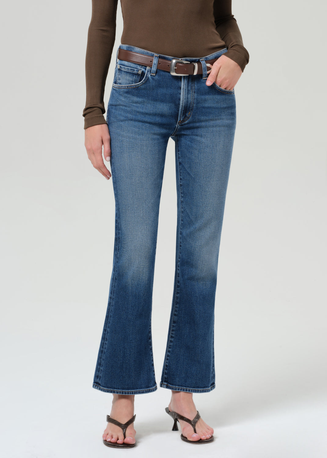 Person wearing a brown long-sleeve shirt and blue jeans on a grey background