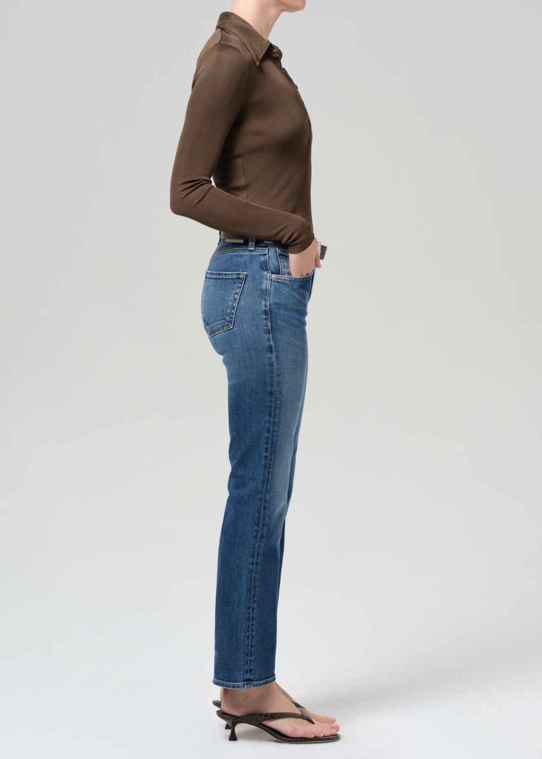 Person wearing a brown long-sleeve shirt and blue jeans on a grey background