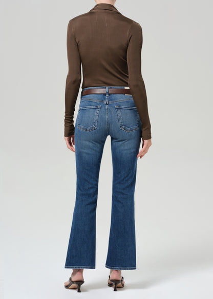 Person wearing a brown long-sleeve shirt and blue jeans on a grey background