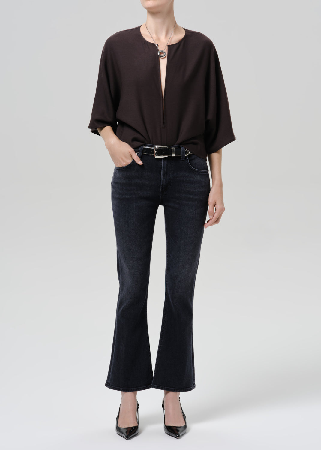 Person wearing a brown shirt with dark blue pants on a grey background
