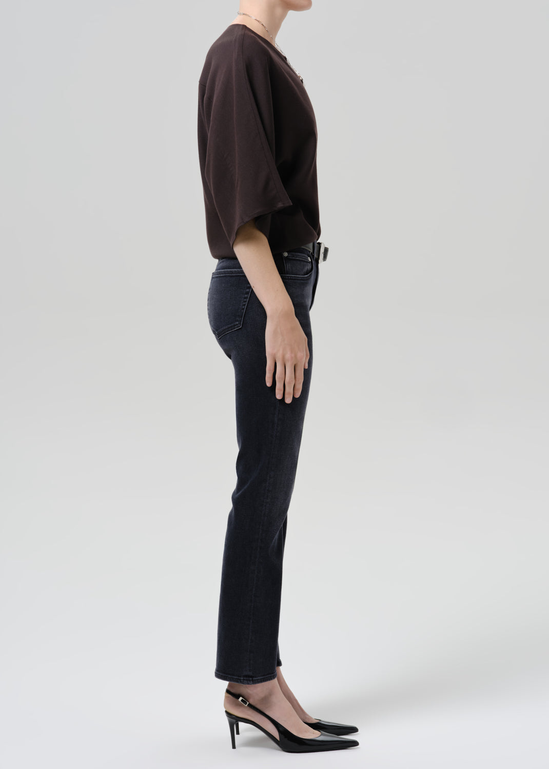 Person wearing a brown shirt with dark blue pants on a grey background