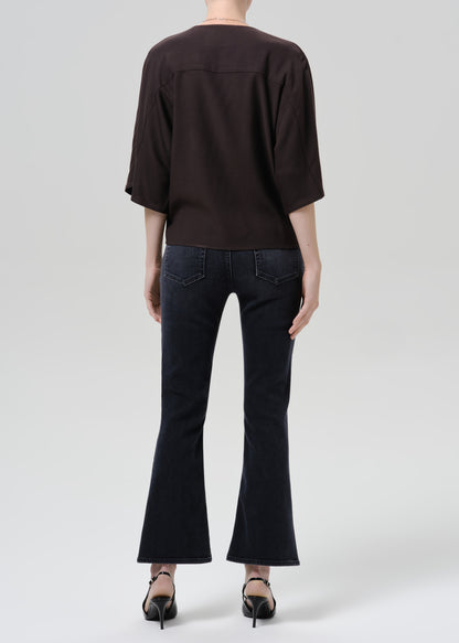 Person wearing a brown shirt with dark blue pants on a grey background