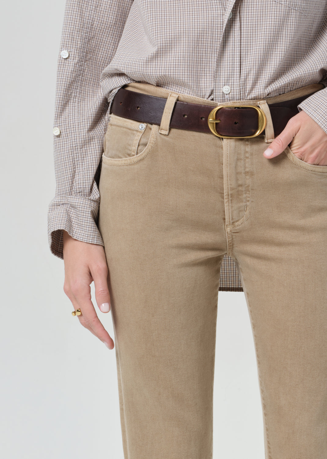 Person wearing a light gray button-up shirt and beige jean on a grey background
