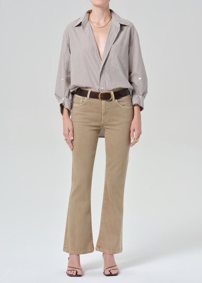 Person wearing a light gray button-up shirt and beige jean on a grey background