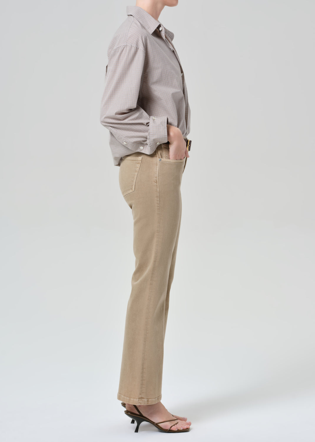 Person wearing a light gray button-up shirt and beige jean on a grey background