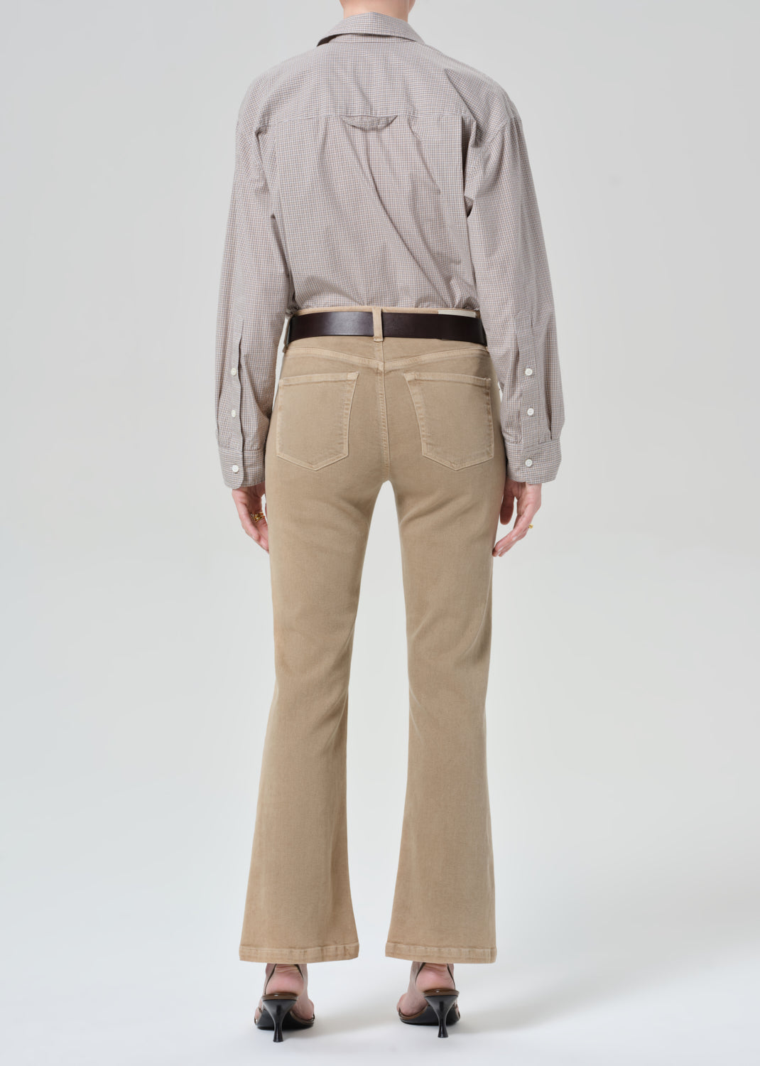 Person wearing a light gray button-up shirt and beige jean on a grey background