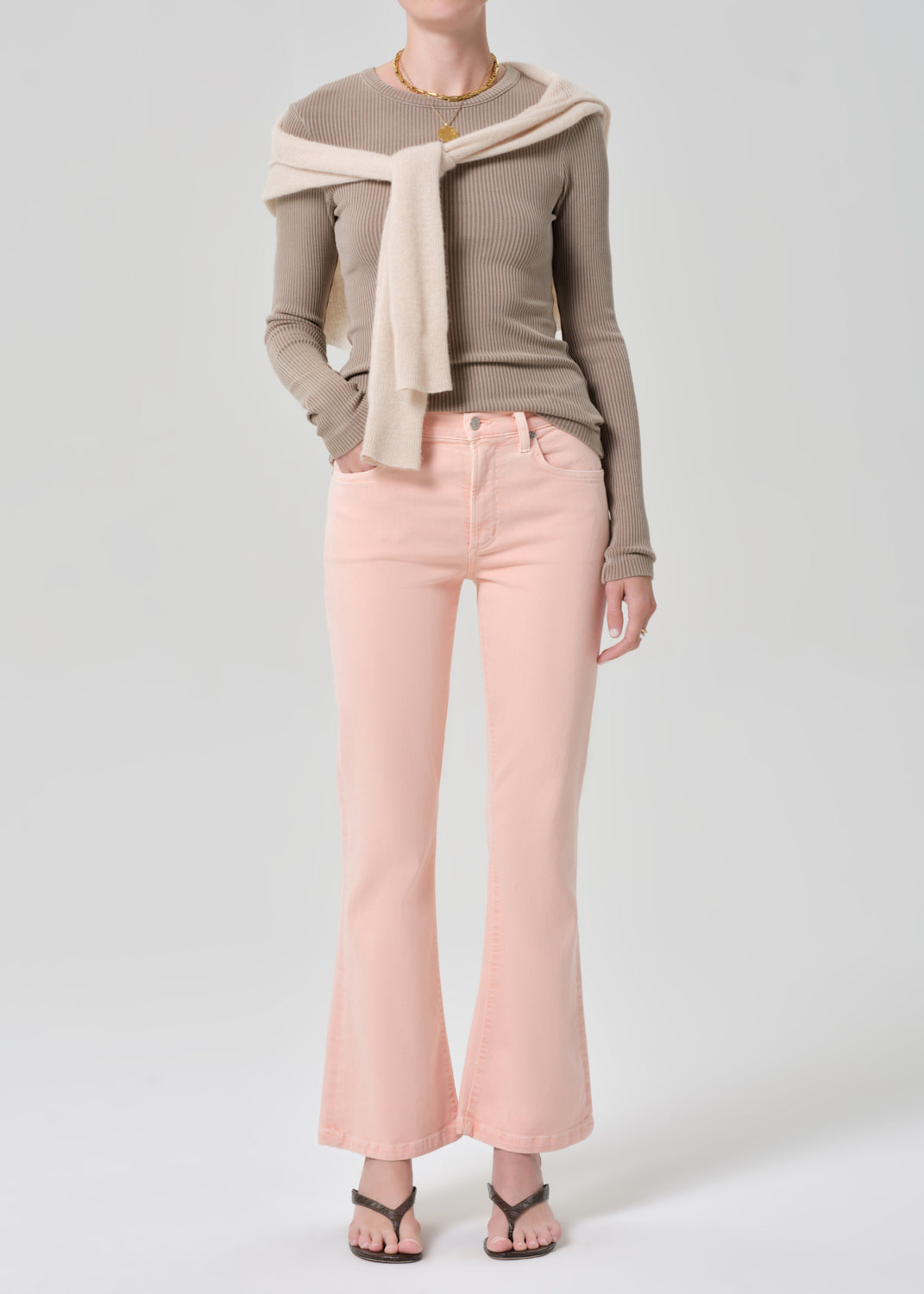 Person wearing a brown top, beige sweater, and pink jeans on a grey background