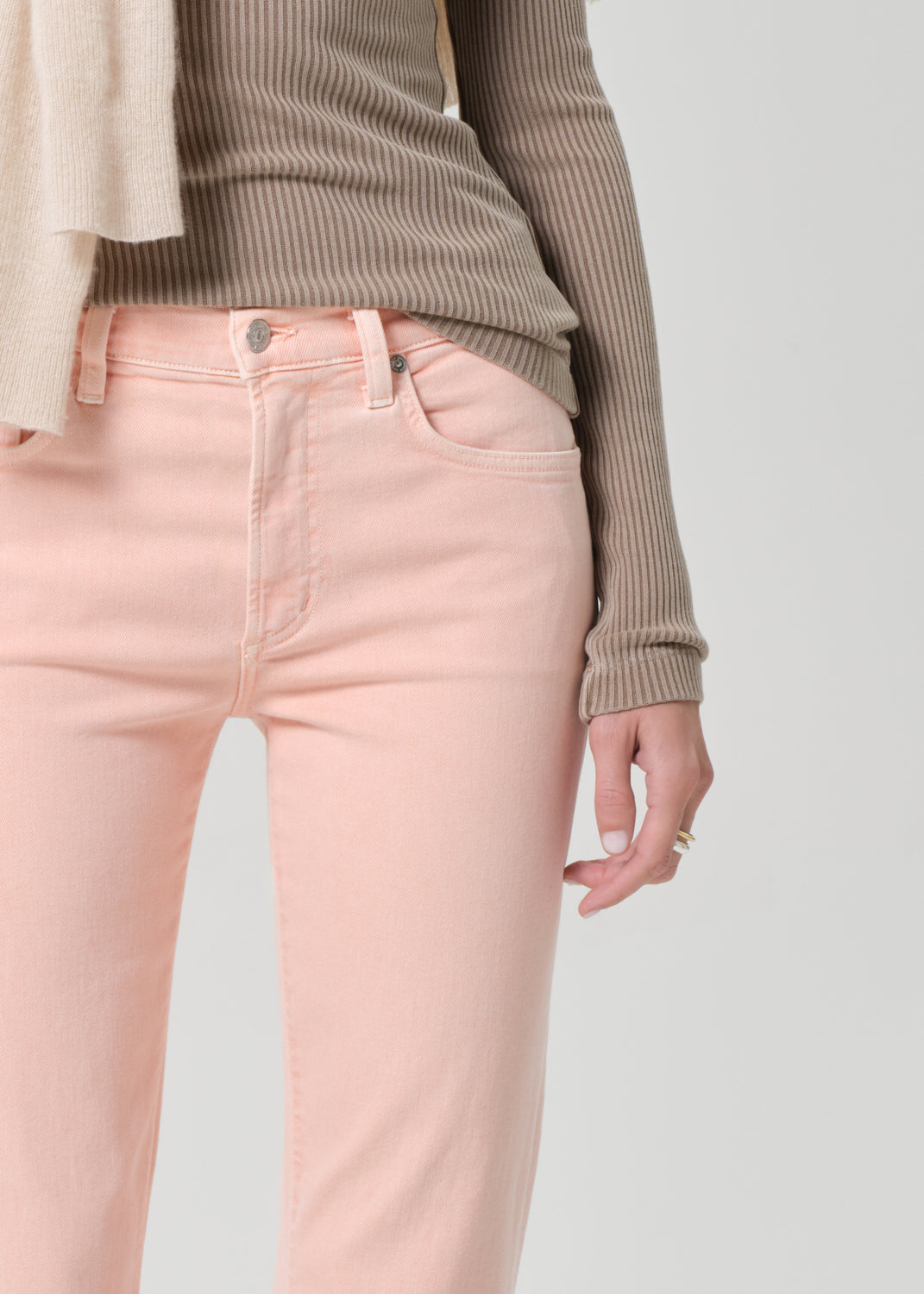 Person wearing a brown top and pink jeans on a grey background