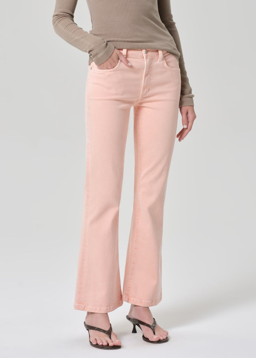 Person wearing a brown top and pink jeans on a grey background