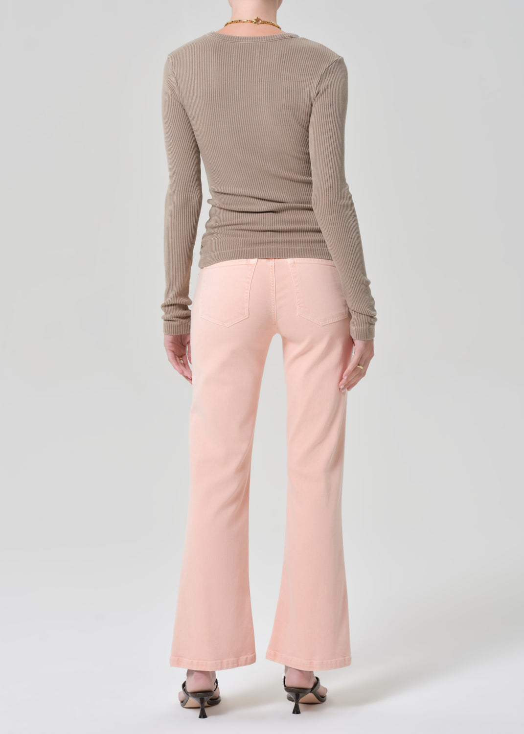 Person wearing a brown top, beige sweater, and pink jeans on a grey background
