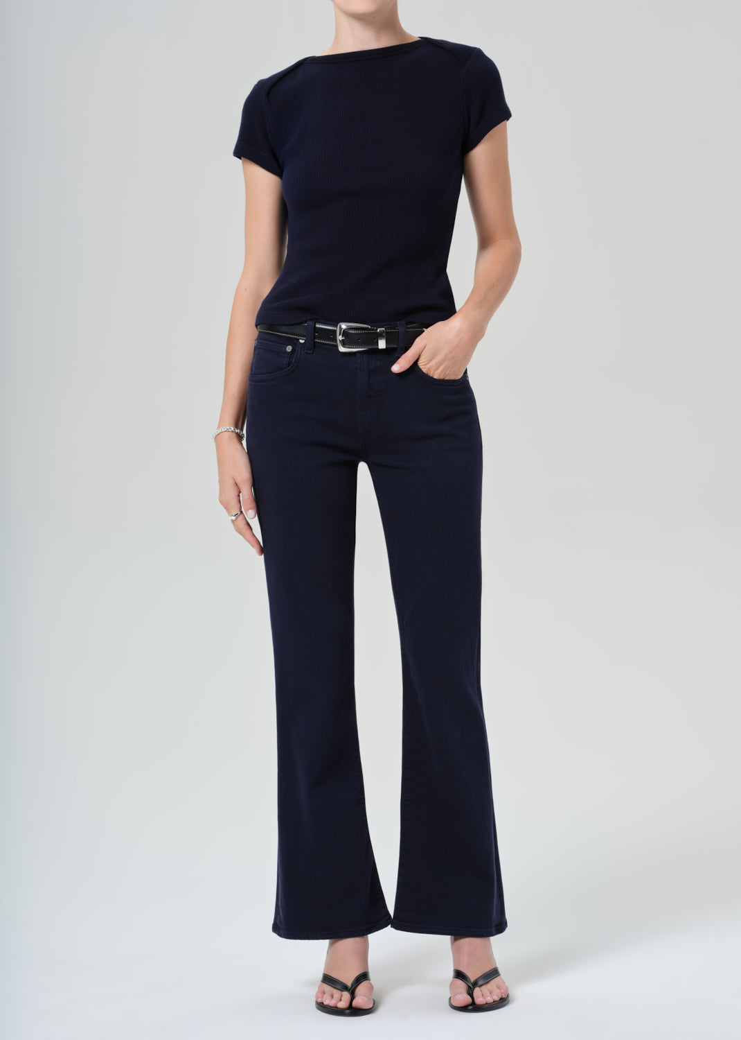 Person wearing a navy t-shirt and dark navy jeans on a grey background