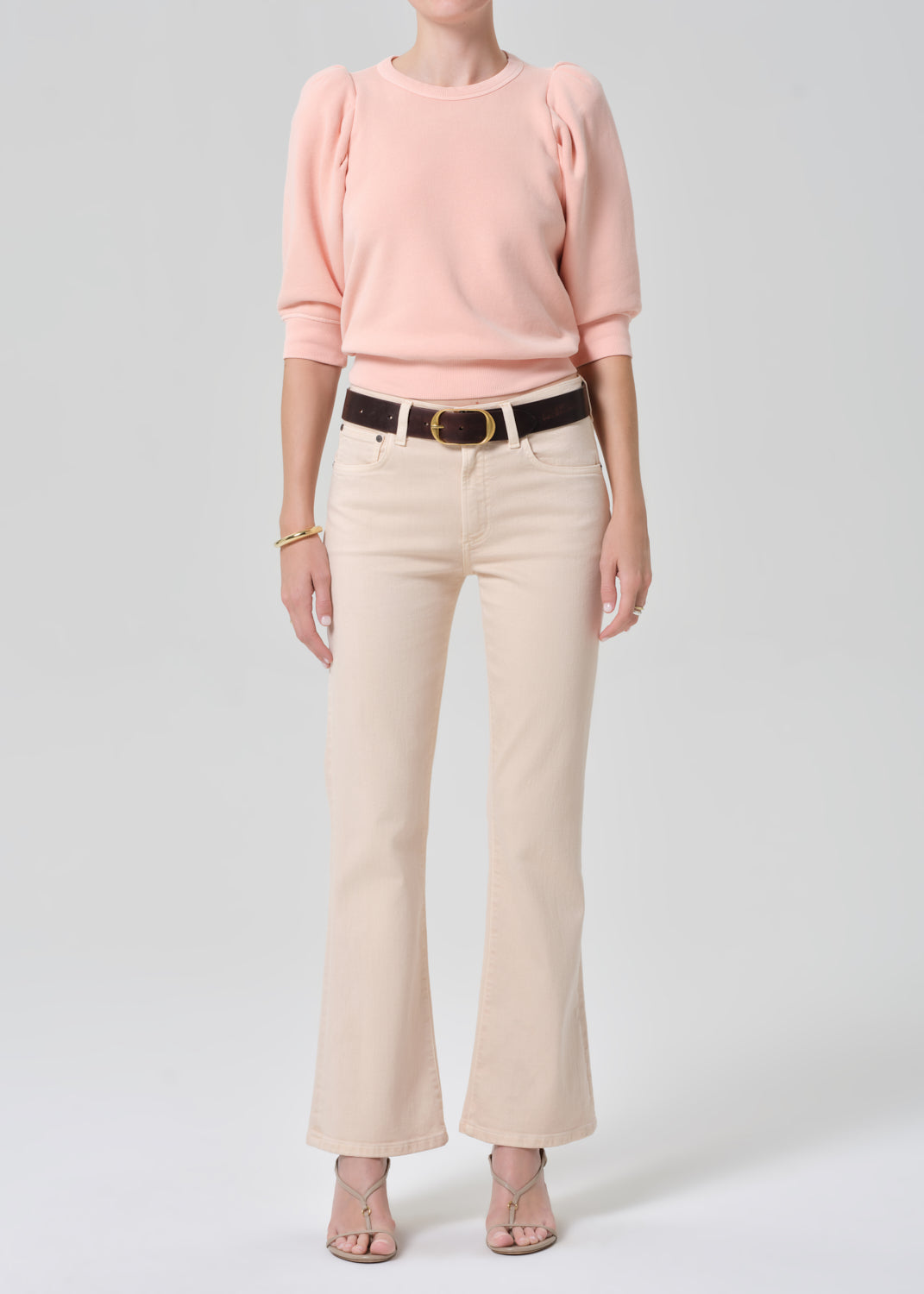 Person wearing a pink sweatshirt and light pink jeans on a grey background