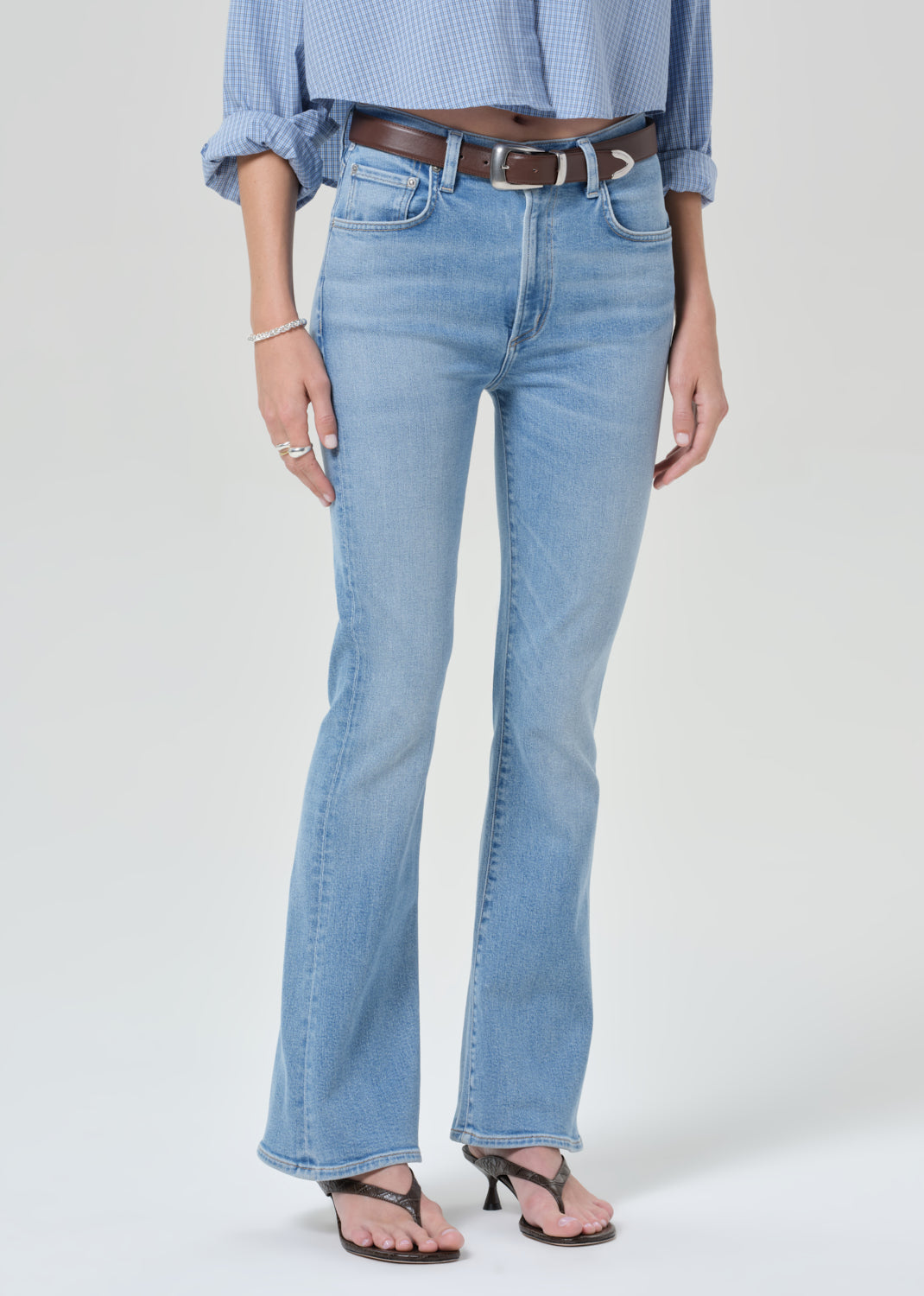 Person wearing a light blue plaid shirt and jeans on a grey background