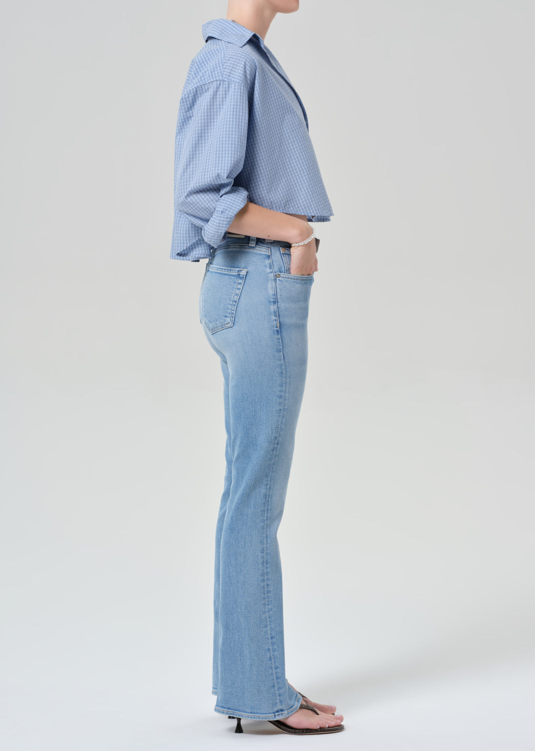 Person wearing a light blue plaid shirt and jeans on a grey background