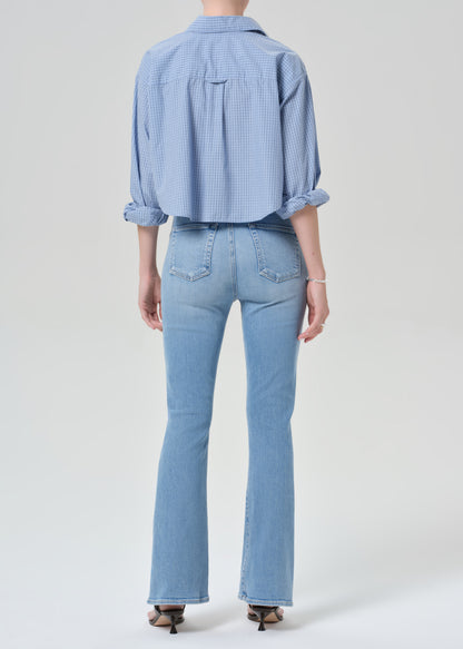 Person wearing a light blue plaid shirt and jeans on a grey background