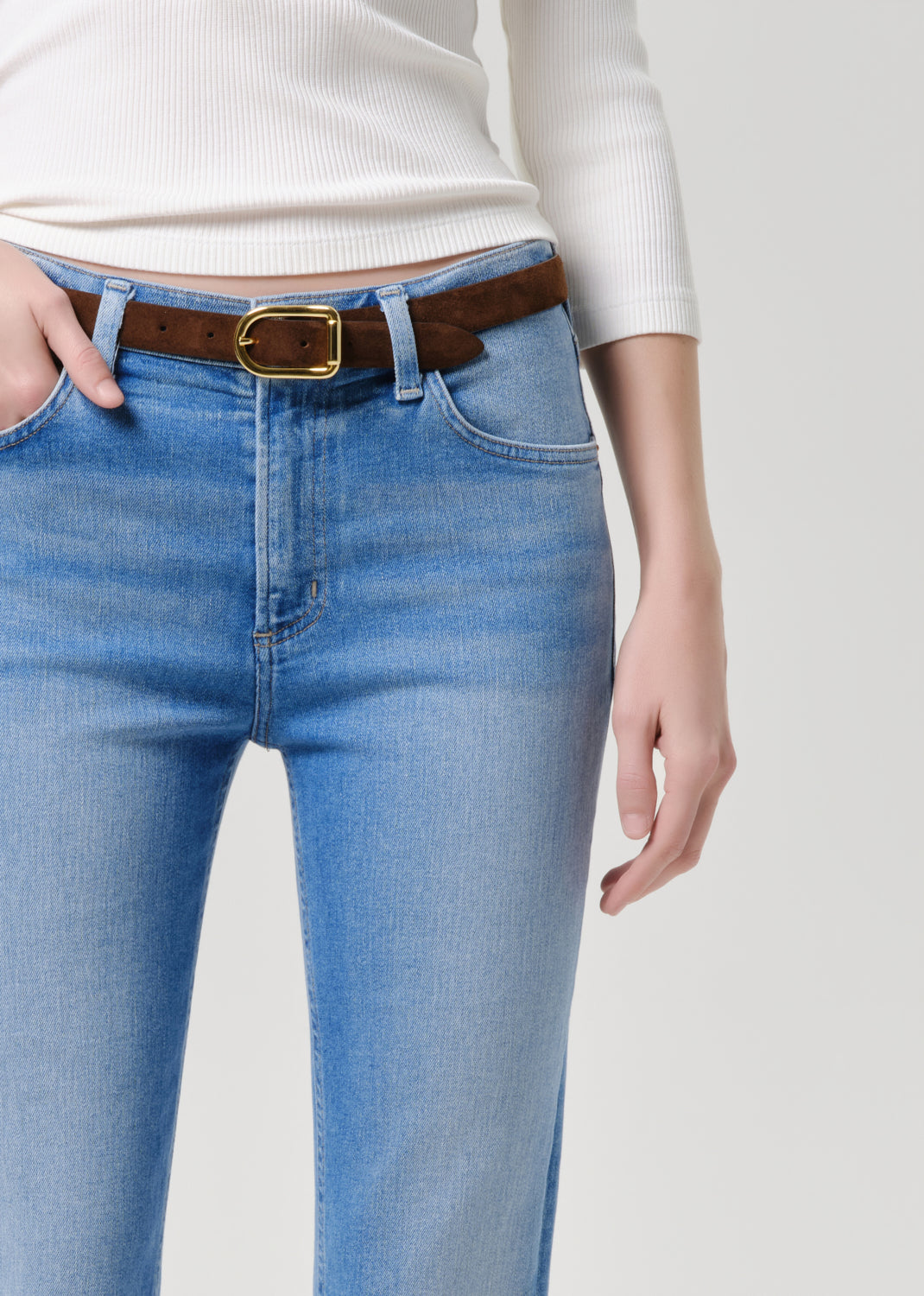 Person wearing blue jeans with a brown belt on a grey background