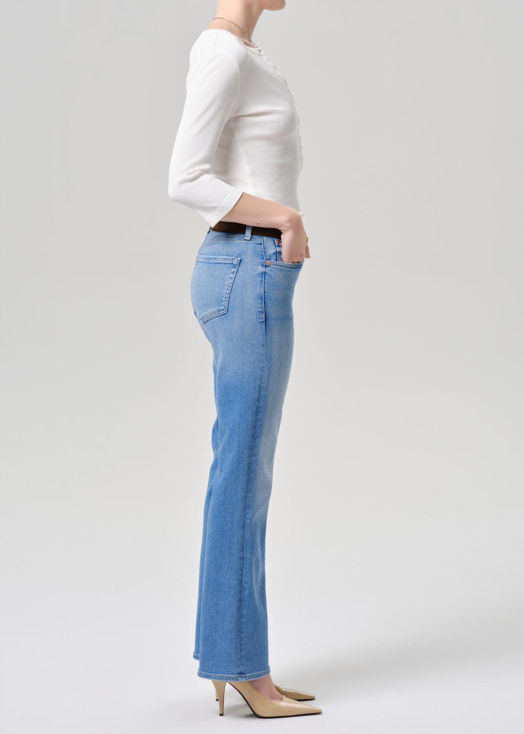 Person wearing light blue jeans and a white top on a grey background