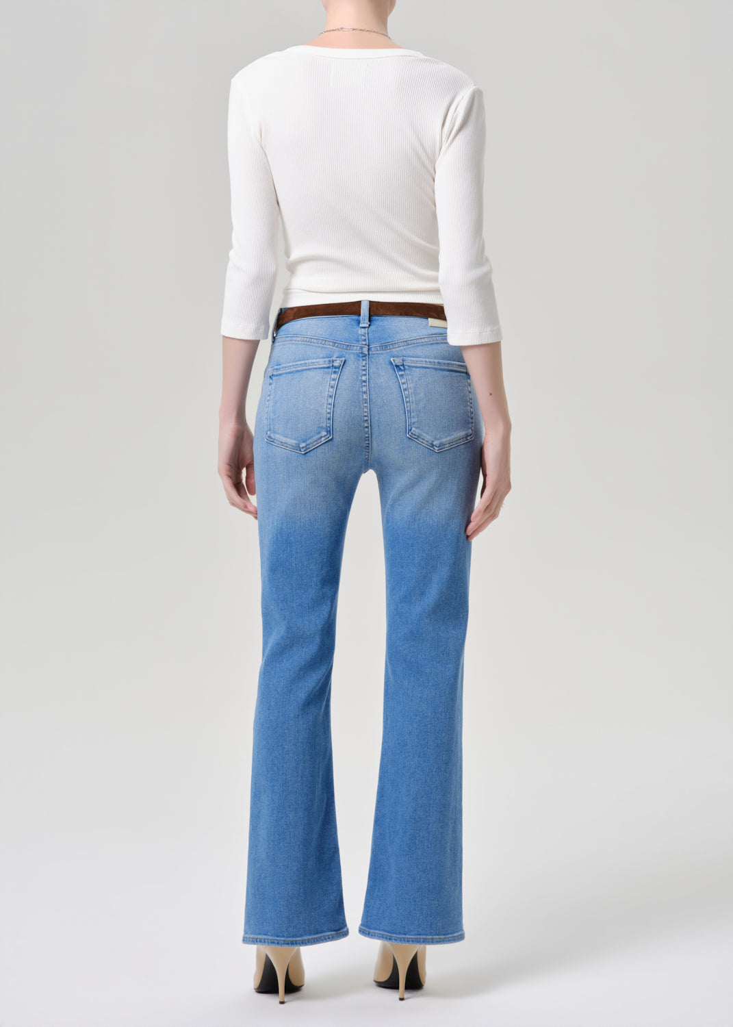Person wearing blue jeans and a white top on a grey background